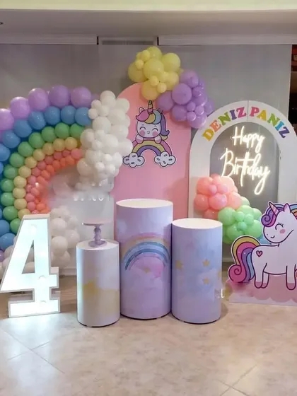 A unicorn and rainbow theme for a 4th birthday. This setup includes themed backdrops, a rainbow balloon arch, a marquee number '4', and a unicorn cutout.