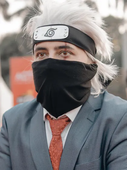 A portrait of a cosplayer as Kakashi Hatake from Naruto, in his formal suit. The shot focuses on the iconic mask and Sharingan eye, key details for any Naruto fan.