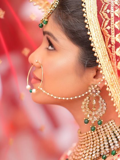 A side-profile portrait of a bride, highlighting her nath (nose ring) and other traditional jewelry against her red veil. This artistic shot captures the elegance of bridal details.
