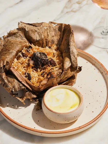 Gucchi Pulao, an aromatic rice dish made with prized morel mushrooms, wrapped and steamed in a lotus leaf to infuse flavor. This is a luxurious vegetarian option available for dine-in or delivery.