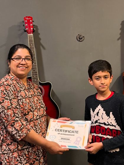 An instructor awards a certificate of achievement to Dharan, celebrating his talent and progress at the school.