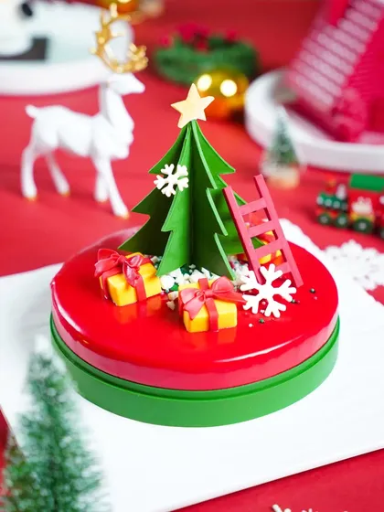 A modern and artistic Christmas cake with a glossy red glaze and a 3D green chocolate tree. The clean, graphic styling against a red background is perfect for a contemporary bakery.