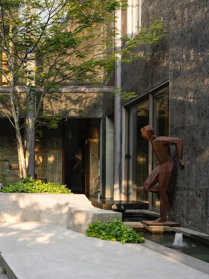 A dynamic bronze sculpture of a figure in motion is placed by a water feature in a modern courtyard. The art piece adds a sense of energy and narrative to the serene space, interacting with the architecture and landscape.