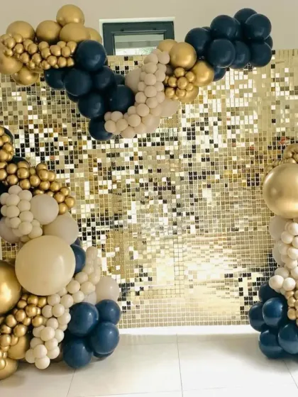 A chic party setup with a gold sequin wall. The balloon arrangement in navy blue, beige, and gold creates a sophisticated and modern color palette.