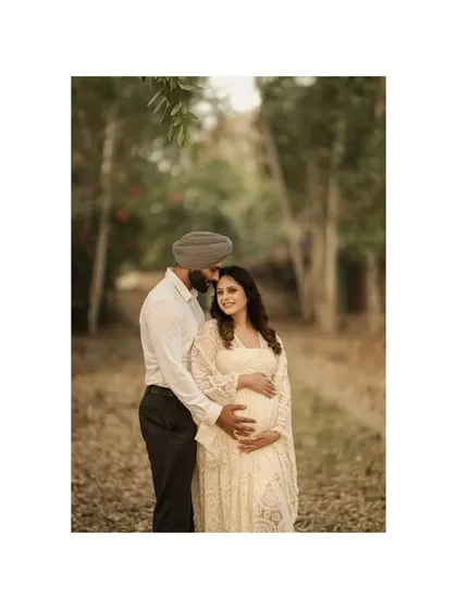 An intimate moment in a woodland setting. The couple stands close together, their connection highlighted by the soft, natural light filtering through the trees.
