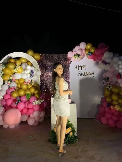 A lovely outdoor birthday setup at night, with a backdrop framed by pink, white, and gold balloons.