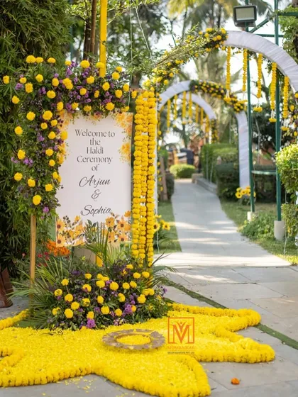 A beautiful welcome sign for a Haldi ceremony, adorned with marigolds and a floral rangoli on the ground. This creates a stunning first impression for guests as they arrive.