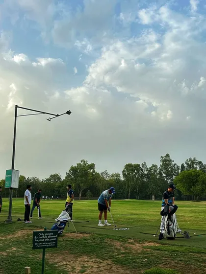 Golfers line the practice area, with their bags creating a colorful display against the green.