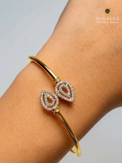 A simple yet elegant gold bracelet with two diamond-studded, paisley-shaped terminals. This open-cuff kada is a versatile piece that can be worn alone or stacked with other bracelets.
