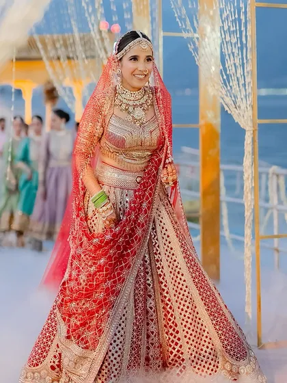A radiant bride making her entrance. Her traditional red Tarun Tahiliani lehenga, paired with a bright red veil, creates a stunning and classic bridal look.