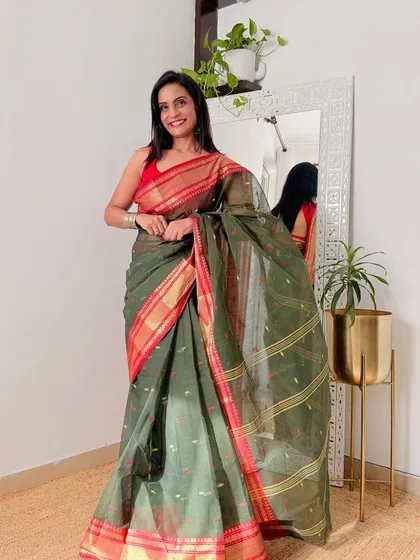 An olive green Tant saree with a contrasting red border. This is a classic color combination that looks very elegant and traditional.