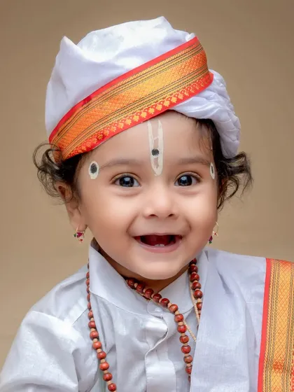 A bright-eyed and smiling close-up of a baby in a Varkari costume. This portrait perfectly captures the happy spirit of a child enjoying the dress-up experience in the studio.
