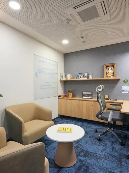 A cozy and functional private office. The space includes a desk, comfortable seating for guests, a whiteboard for brainstorming, and shelving for personal items.