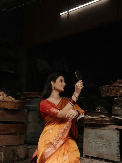A wider shot of the scene, capturing the atmosphere of the old market as the model in her saree admires her reflection.