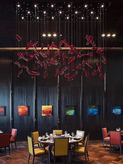 A modern restaurant interior within the Sheraton. A suspended art installation of red glass elements acts as a chandelier, creating a vibrant and artistic focal point above the dining tables.