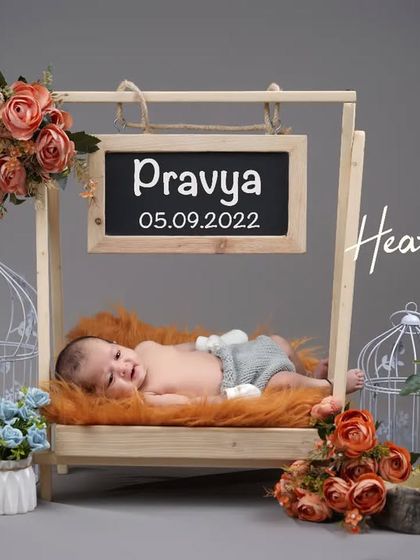 A happy smile from a baby boy relaxing in a wooden swing prop. The personalized chalkboard with his name and birthdate adds a special touch to this milestone photo.