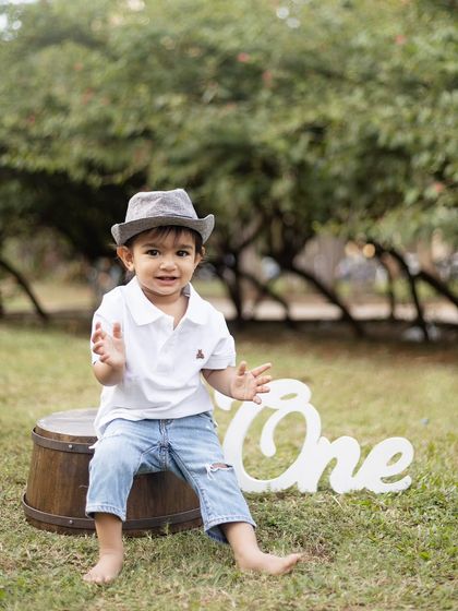 A happy, clapping moment from the one-year-old, sitting on a rustic barrel prop in the park.