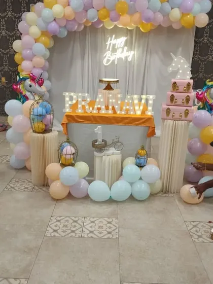 A pastel unicorn theme setup in progress, showing the arrangement of pedestals and a soft-colored balloon arch.