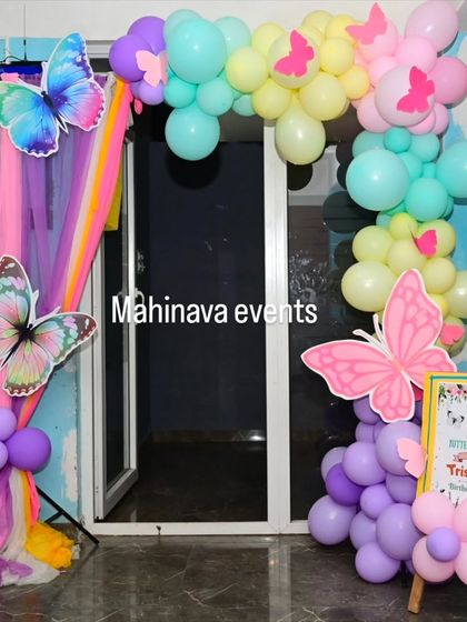 A clear, bright photo of the rainbow butterfly entrance decor. The design includes a mix of pastel balloons, sheer drapes, and a small welcome easel, perfect for a daytime party.