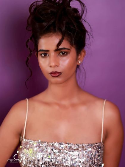 A direct and confident portrait against a purple background. The lighting is clean, and her expression is powerful.