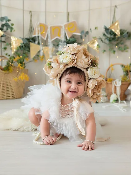 This image showcases the large floral bonnet and the white wood-panel backdrop used in a sitter session. The wicker baskets and greenery in the background are also part of my prop collection.