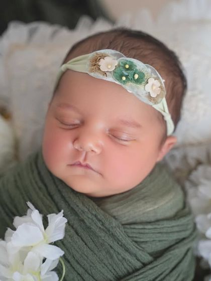 A perfect close-up of a sleeping baby's face, showing off her chubby cheeks and the delicate details of her floral headband.
