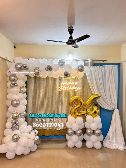 A 24th birthday celebration with a white and silver balloon arch. The setup includes a shimmer curtain and foil number balloons.