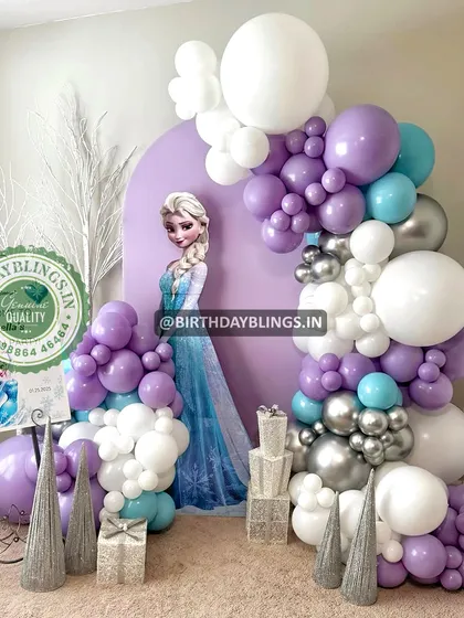 An elegant Frozen theme featuring a purple backdrop and a sophisticated balloon arch in shades of purple, white, and silver. The stacked gift boxes and welcome sign add a touch of class.