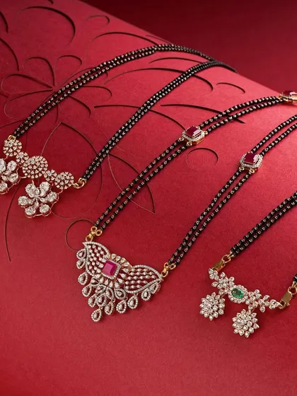 A collection of modern mangalsutra designs. The rich red, textured background provides a beautiful contrast to the gold, diamonds, and black beads, creating a warm and inviting group shot.