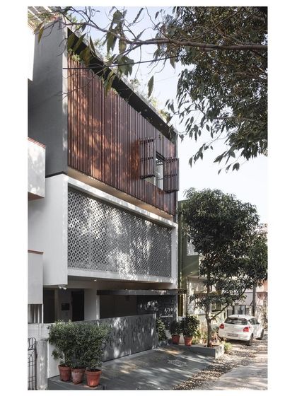 The full facade of the '10x10 Residence'. The design stacks different textures and patterns, from the perforated gate to the concrete jaali and the upper wooden screen, creating a rich and layered urban home.