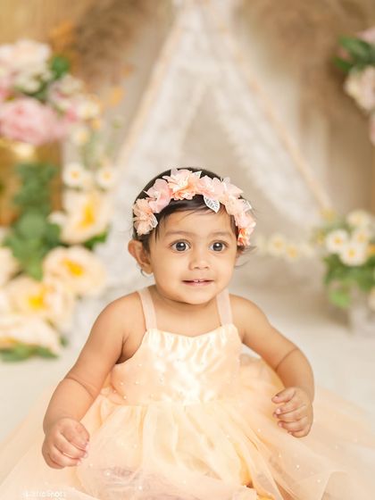 A sweet and curious expression from a little girl in a peach dress. The soft, dreamy background with flowers and a teepee creates a beautiful boho-chic vibe.