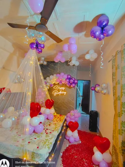 Another angle of the purple-themed birthday room, showing the balloon arch and the rose petal pathway. The mix of purple, white, and silver balloons gives it a unique and stylish look.