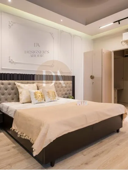 A completed master bedroom project, featuring a tufted headboard with a fluted wood frame, set against a wall with ornate molding. The light wood flooring and neutral wardrobes keep the space feeling bright and airy.