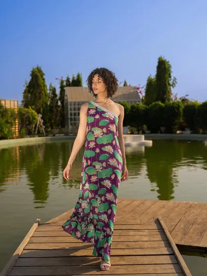 An outdoor campaign shot for Tangerine Tiger by a lakeside. The natural lighting and serene environment complement the flowing, one-shoulder printed dress.