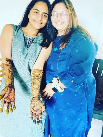 A happy client posing with her friend, showing the beautiful result of her bridal mehndi session.
