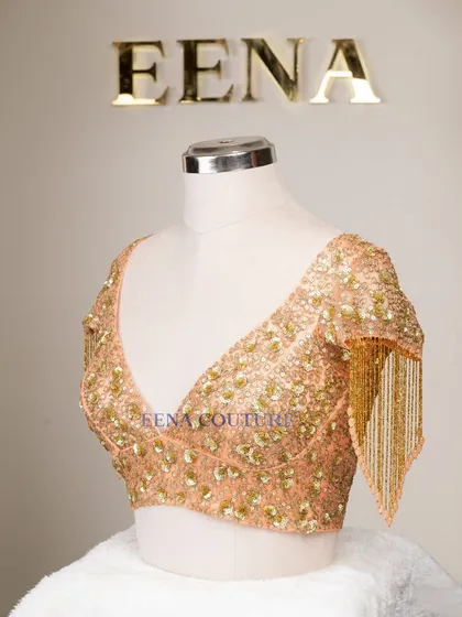 This peach-toned blouse is all about the sparkle and movement. It's crafted from net and covered in sequin and zardozi floral motifs, with dramatic, dangling beaded tassels on the sleeves for a show-stopping effect.