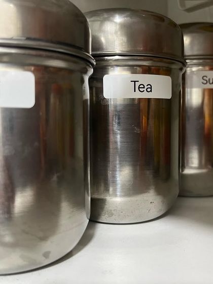 For a classic Indian kitchen, labeled steel dabbas are a practical and durable solution. Here, we've organized the tea corner with clearly labeled containers for ilachi, tea, and sugar.