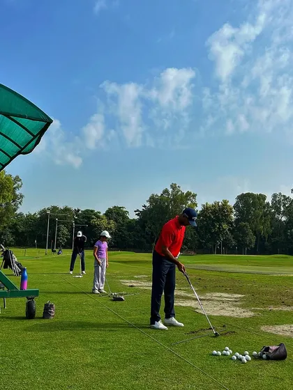 A golfer prepares for his next shot from the practice mat, with others spread out across the range on a beautiful day.