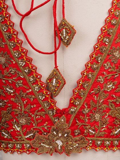 This sleeveless red blouse is perfect for a bold bridal statement. It features a deep V-neckline and is heavily embellished with intricate gold floral zardozi work, creating a rich and luxurious feel.