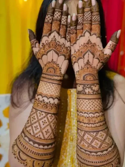 A happy client showing off her beautiful Teej mehndi. The festive background adds to the celebratory mood.