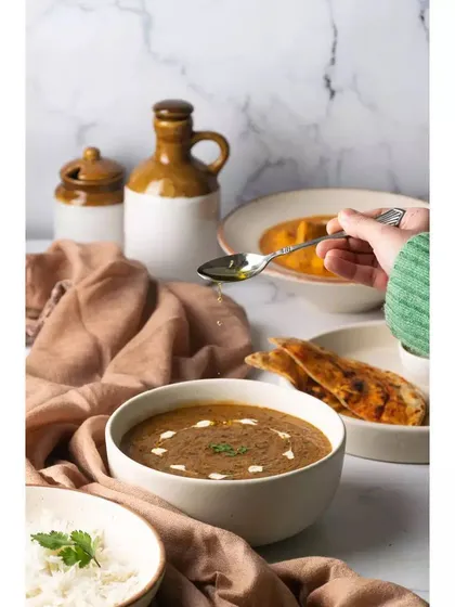A moment captured as ghee is drizzled over a bowl of dal. This action shot adds a dynamic and appetizing element to the scene, highlighting the richness of the dish.