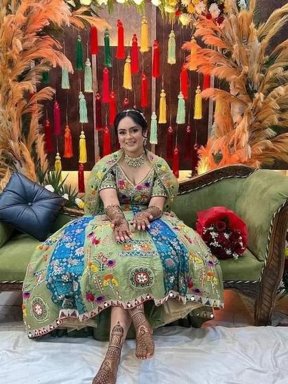 A beautiful bride at her mehndi ceremony, looking regal on a green sofa with her hands and feet adorned with our art.