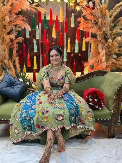 A beautiful bride at her mehndi ceremony, looking regal on a green sofa with her hands and feet adorned with our art.