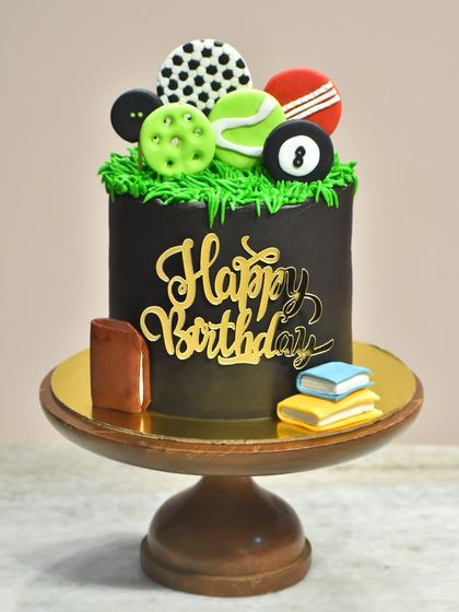 A unique cake for someone who loves both sports and books. This design features a variety of fondant sports balls on top and miniature edible books at the base.