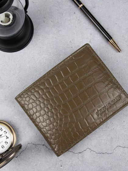 A styled flat-lay of the green crocodile wallet with a pocket watch and pen.