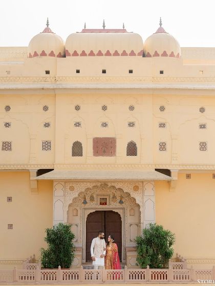 A wide-angle portrait of the couple standing before the magnificent facade of Mundota Palace.