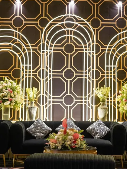 A chic lounge area designed with modern black sofas set against a geometric, art-deco-inspired backdrop. The glowing arches and fresh flowers added softness and elegance.