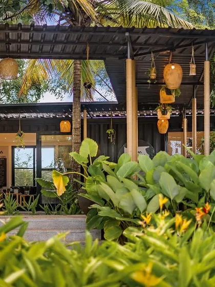 The exterior of the container marketing office, surrounded by lush tropical plants. The industrial look of the container is softened by the warm lighting and natural elements, creating an inviting entrance.