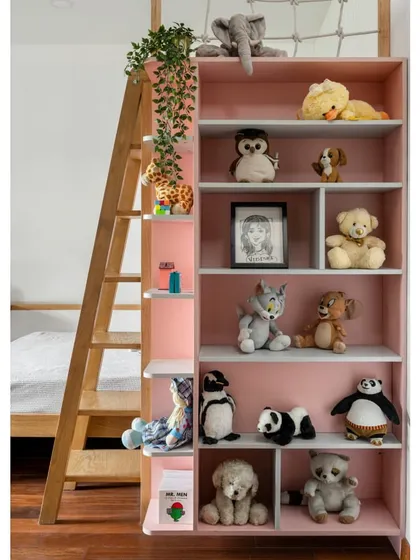 A tall, open bookshelf in a soft pink finish provides ample storage for toys and books in the 'Vasudhalayah' daughters' room.