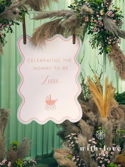 The welcome sign for the baby shower, framed by pampas grass and delicate pink flowers.